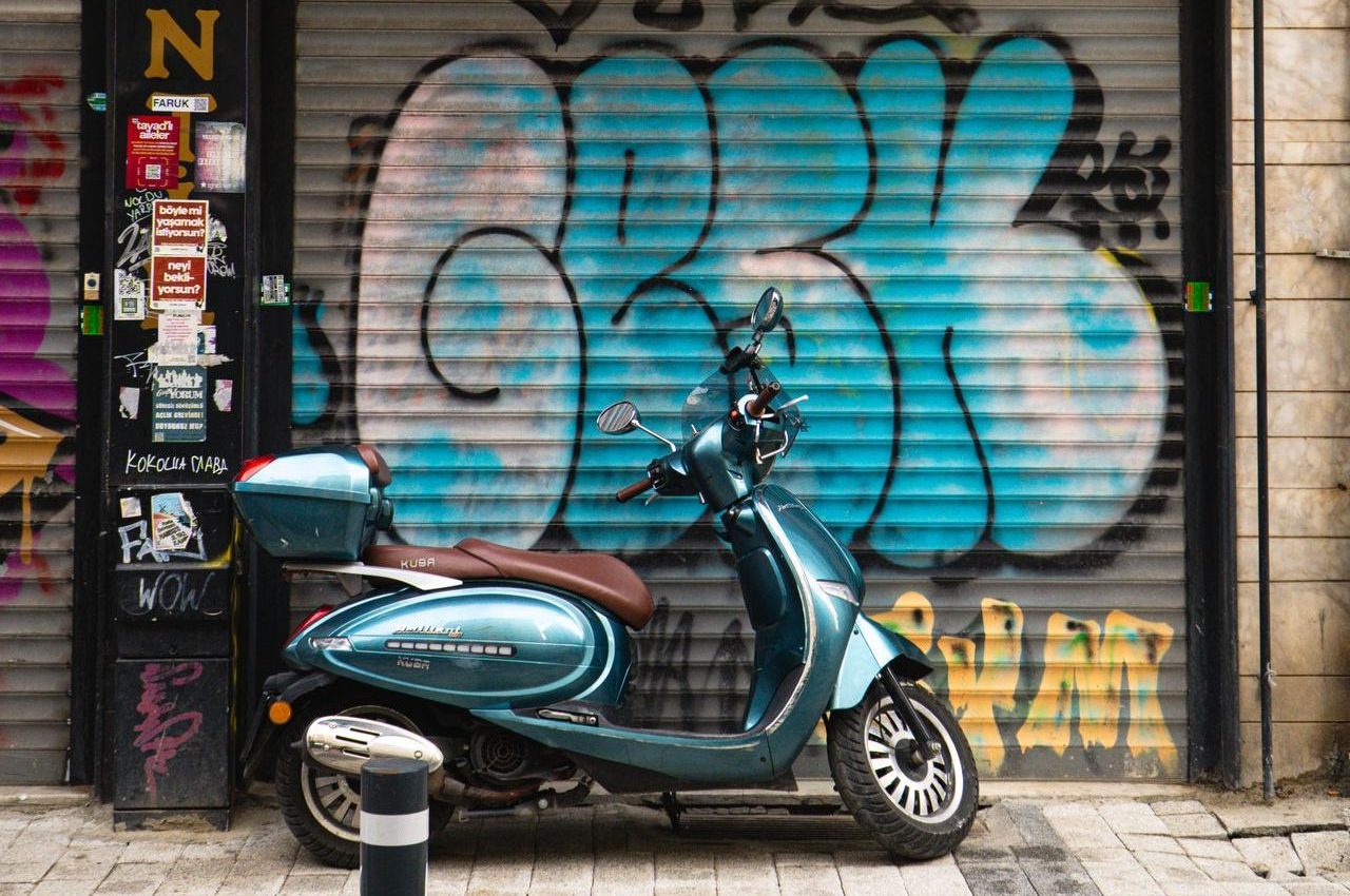 A photograph of a motorbike parked in front of a metal shutter decorated in graffiti