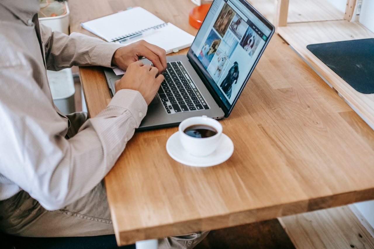 Photograph of a person sat at a desk using a laptop with a mug of tea or coffee beside them