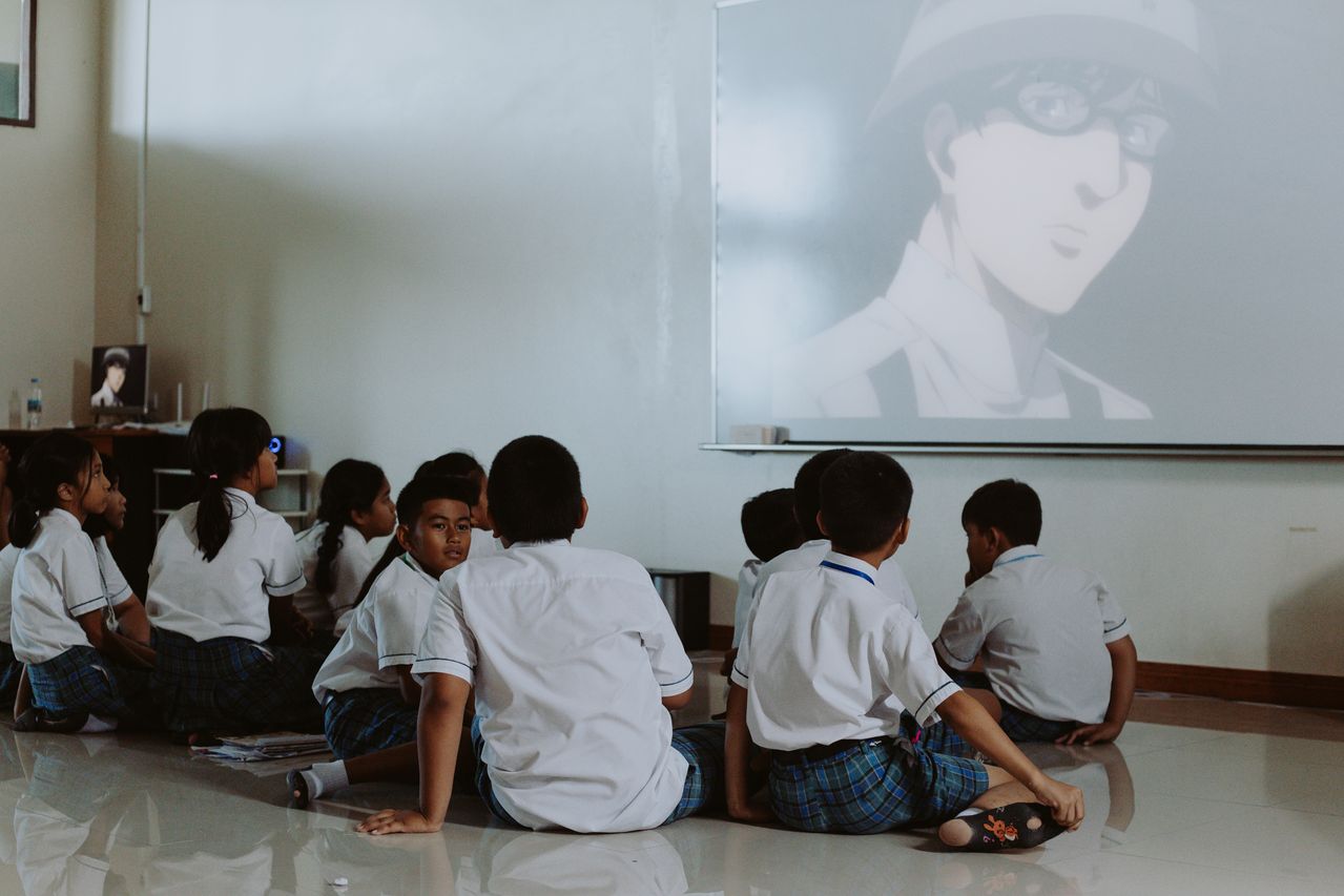 Photograph showing students sat on the floor watching a projected video on the wall in a classroom